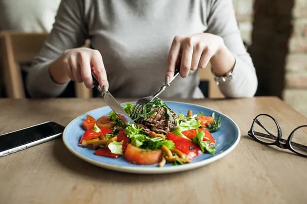 A hand holding a wooden cutting board with various healthy vegetables, fruits, and herbs like broccoli, avocado, lemon, and ginger, symbolizing a healthy diet.